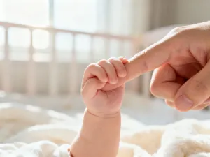 Niemowlęca dłoń sięgająca po kolorową drewnianą zabawkę w przytulnym pokoju dziecięcym.